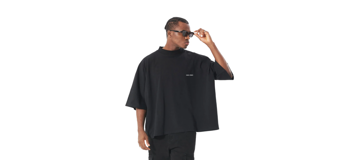 Man wearing oversized black t-shirt made from sustainable materials adjusting sunglasses on white background