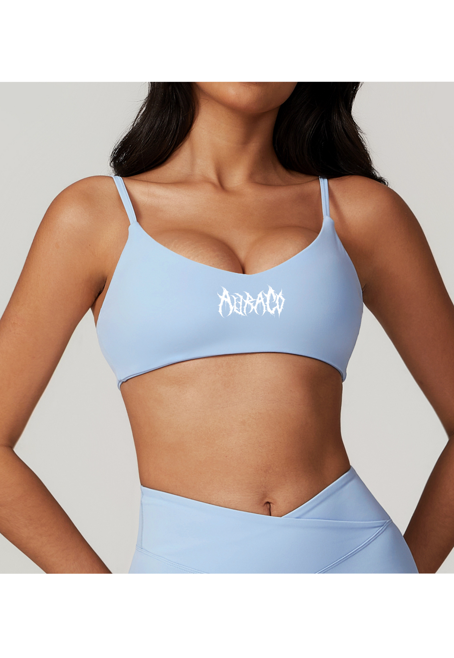 Woman wearing light blue AuraCo Sports bra with white logo and thin straps, designed for medium support and breathability